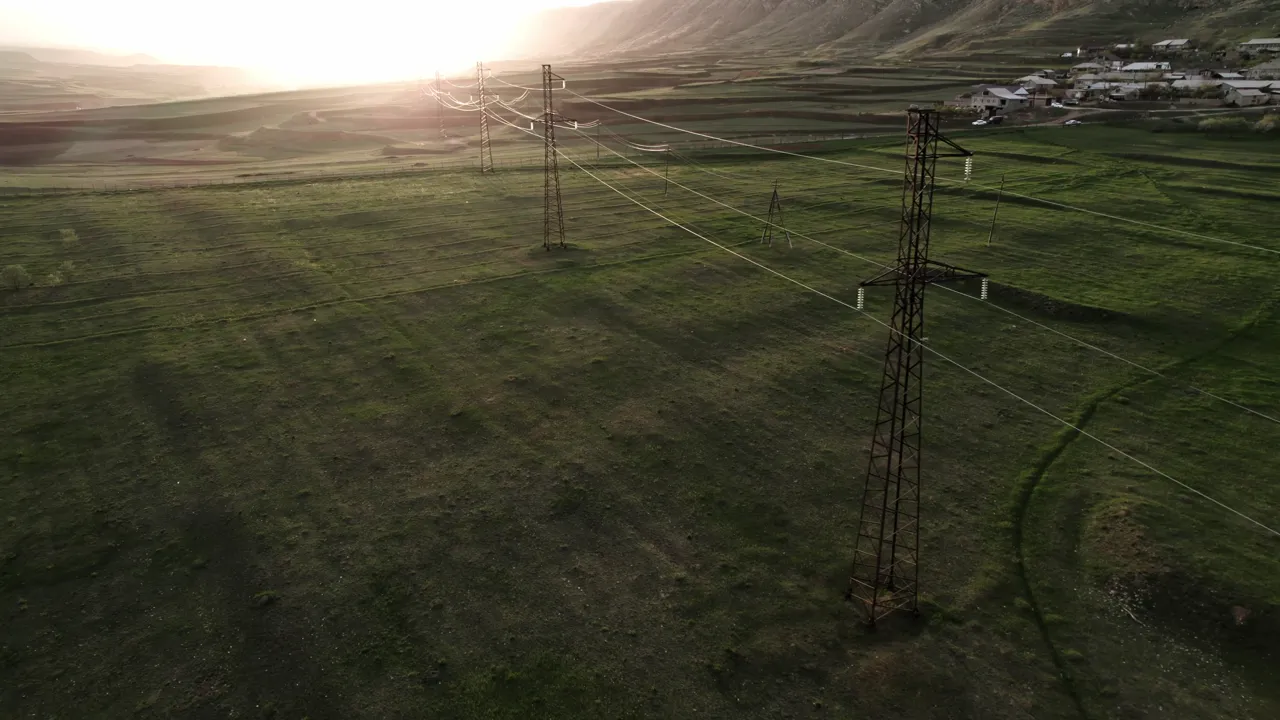 Transmission lines crossing open land in the evening light.